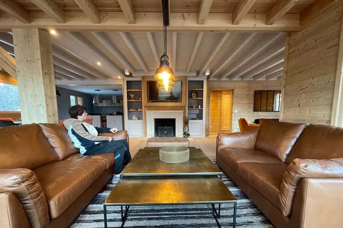 A man sits on a brown leather couch in a living room