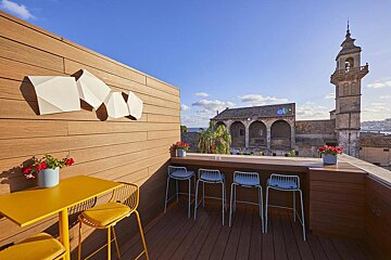 A balcony with a table and stools and a tower in the background