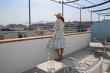 A woman in a floral dress stands on a balcony overlooking a city