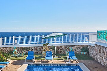 A swimming pool with blue chairs and an umbrella overlooking the ocean