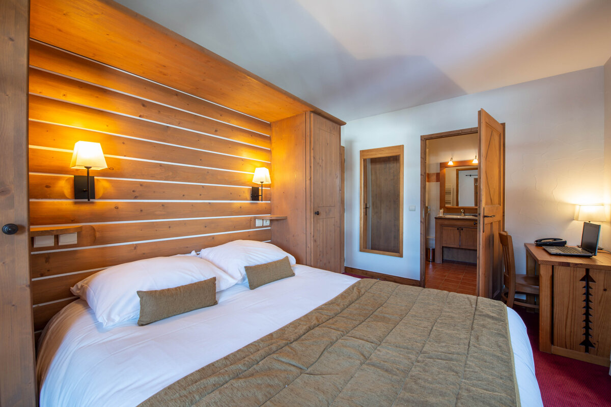 A bedroom with a bed and a desk with a laptop on it