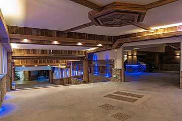 A luxurious underground parking garage with rustic wooden beams and walls, illuminated by warm ceiling lights and striking blue LED accents along ramps and a parked car.