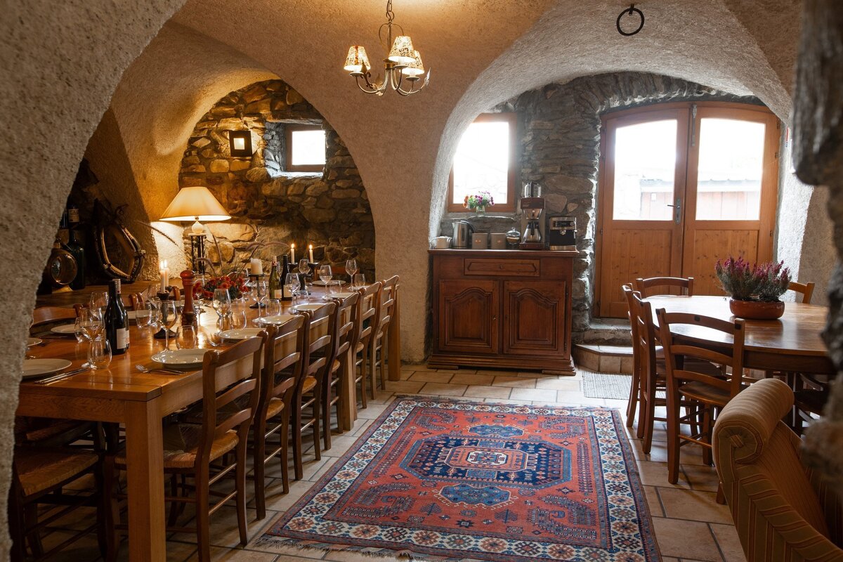 A charming, rustic dining room with vaulted ceilings, stone walls, and a long table set with candles, creating a warm, inviting atmosphere.