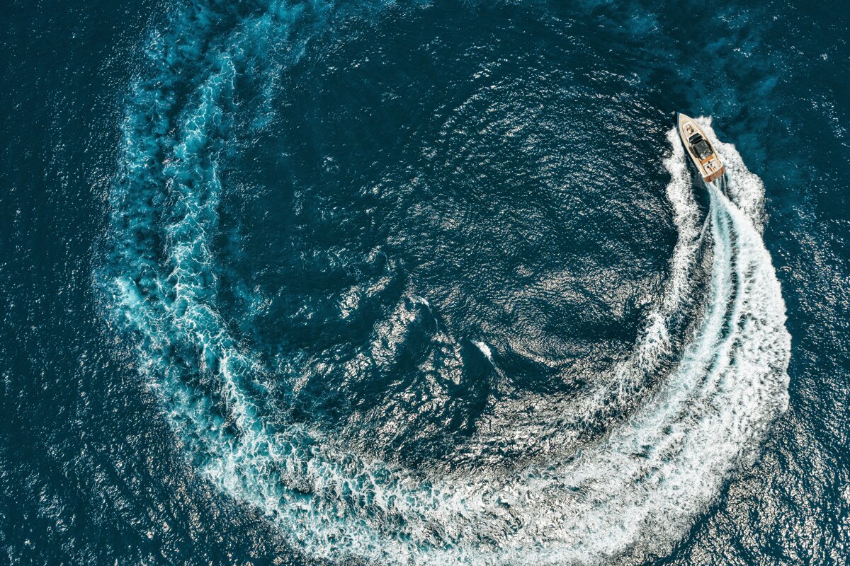 Aerial view of a boat cruising in a circle on deep blue water, creating a large, circular white wake.