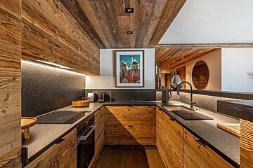 A modern U-shaped kitchen with rustic wooden cabinets, ceiling, and dark stone countertops. Features under-cabinet lighting and contemporary appliances.