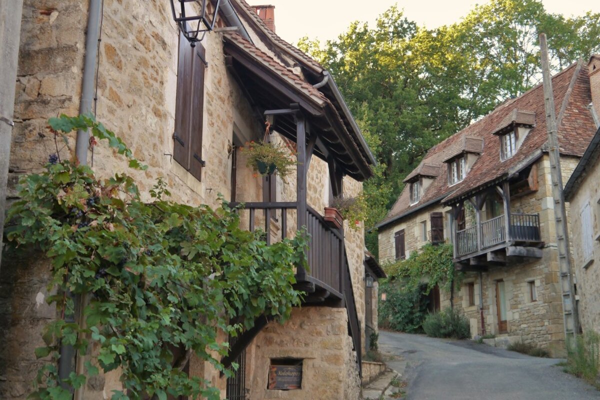 looking up a street with houses & timber balconies, Carennac