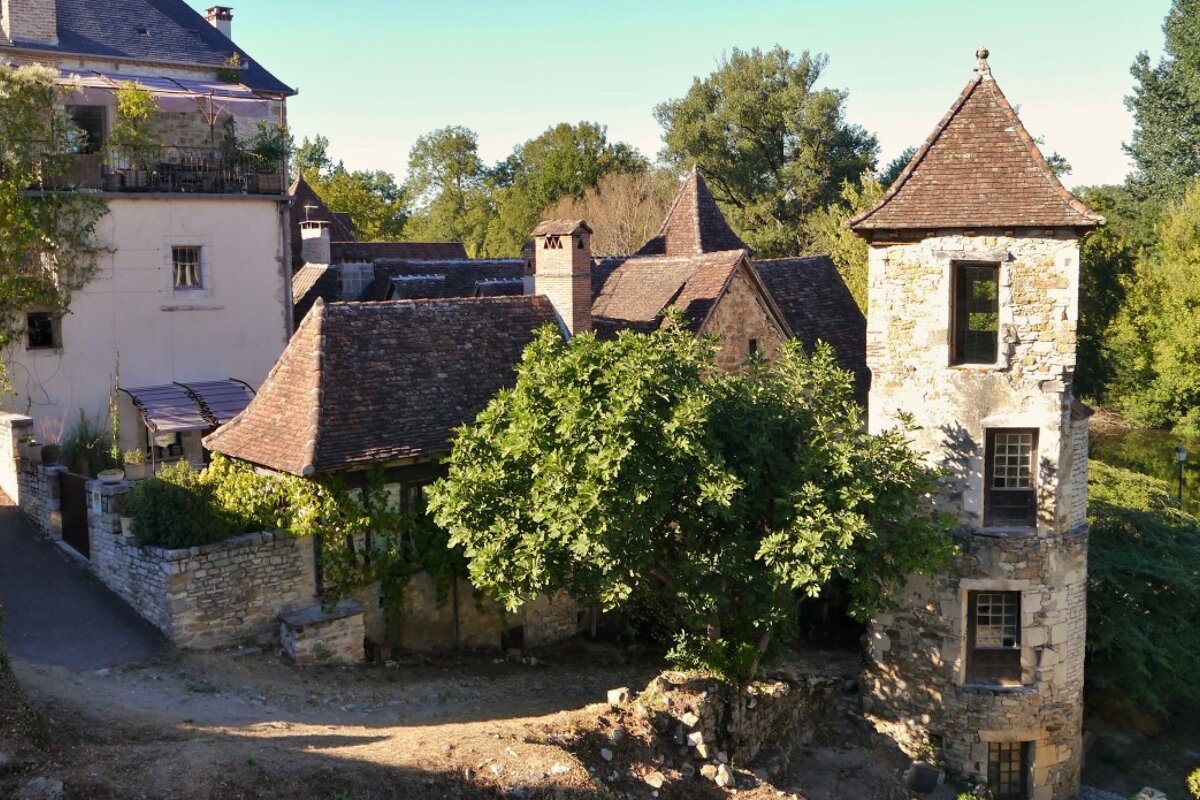 some buildings and trees by a river in carennac