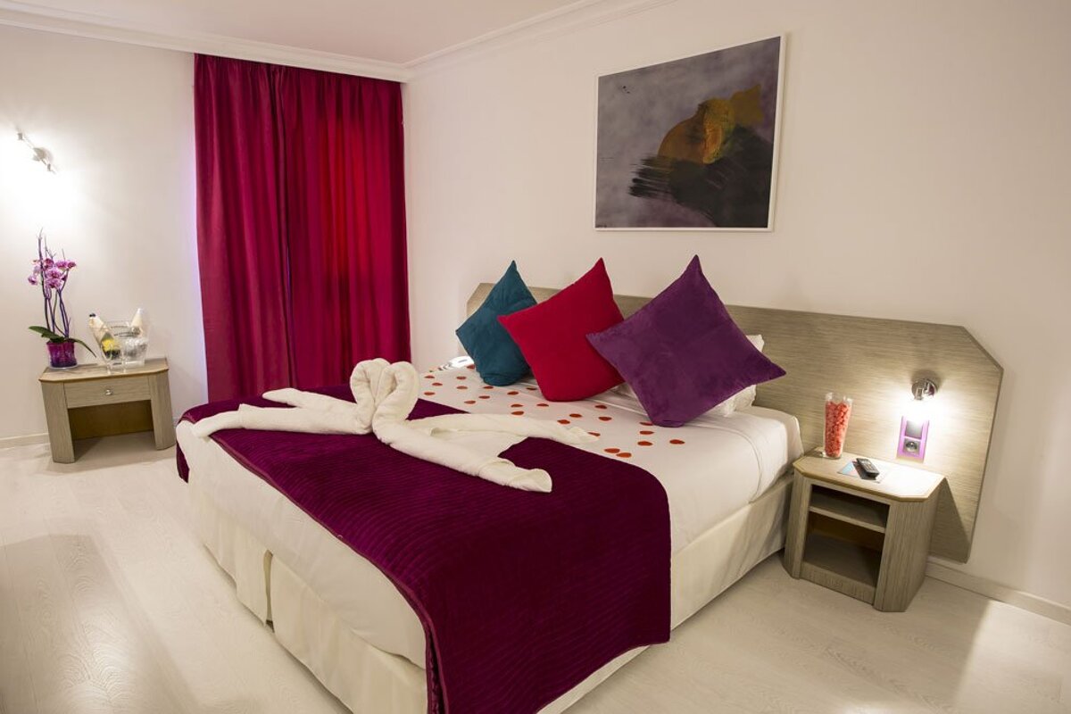 A hotel room with a bed decorated with purple blankets and pillows
