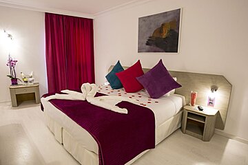 A hotel room with a bed decorated with purple blankets and pillows