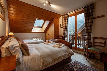 A cozy attic bedroom with wooden ceilings, a double bed, a single bed, a skylight, and a balcony overlooking lush mountains.
