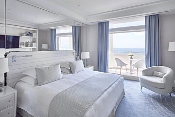 A bedroom with a large bed and a balcony overlooking the ocean