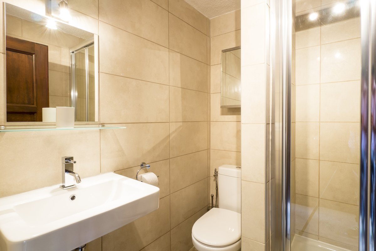 Modern beige-tiled bathroom with a white sink, toilet, mirror, and a glass-enclosed shower.