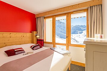 A bedroom with a bed and a window with mountains in the background
