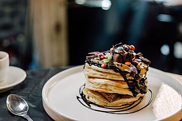 A stack of pancakes with chocolate sauce and candy on top