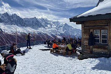 A group of people sitting at tables in the snow with mountains in the background