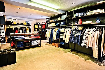 A brightly lit clothing store showcases racks of jackets, folded apparel, hats, and bags on shelves and tables, creating a neat retail display.