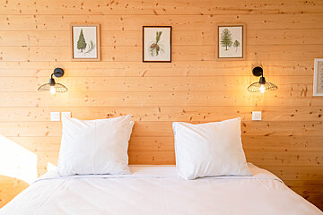 A bed with white sheets and pillows against a wooden wall