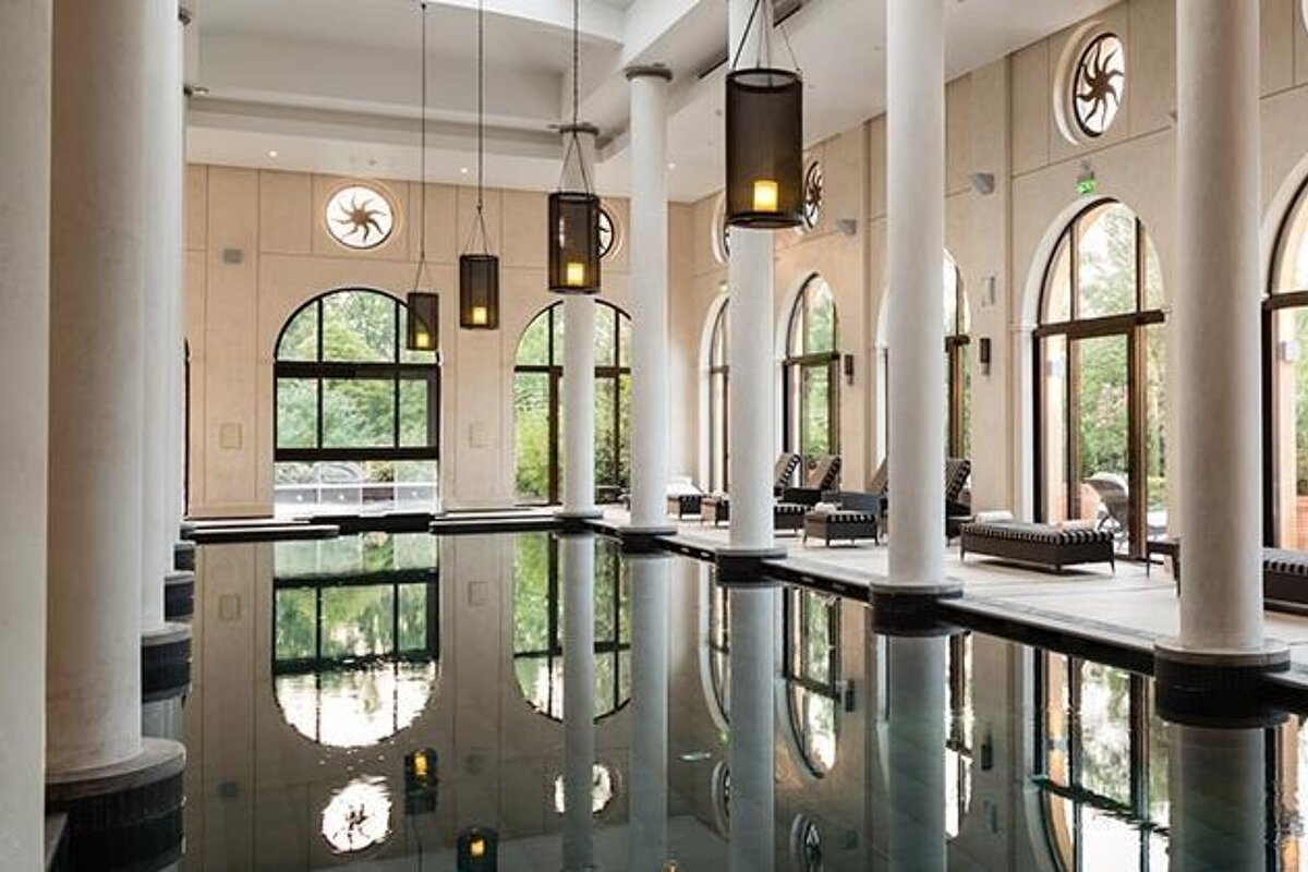 image of an indoor swimming pool in a grand building with tall stone columns, large windows and sunbeds