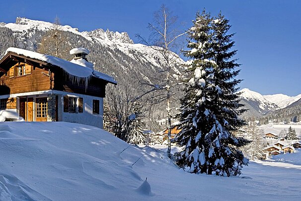 A snowy mountain landscape with a cabin in the foreground