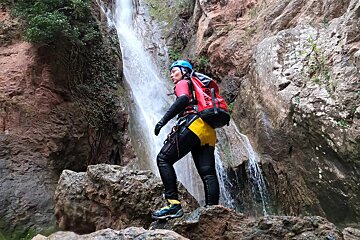 A person standing in front of a waterfall with a red bag that says ' salomon ' on it