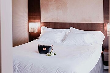 A bed with white sheets and pillows and a black bag on it