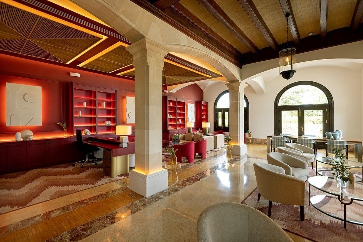 Elegant and expansive room combining red accent walls, stone pillars, patterned wooden ceilings, and various seating areas under arched windows.