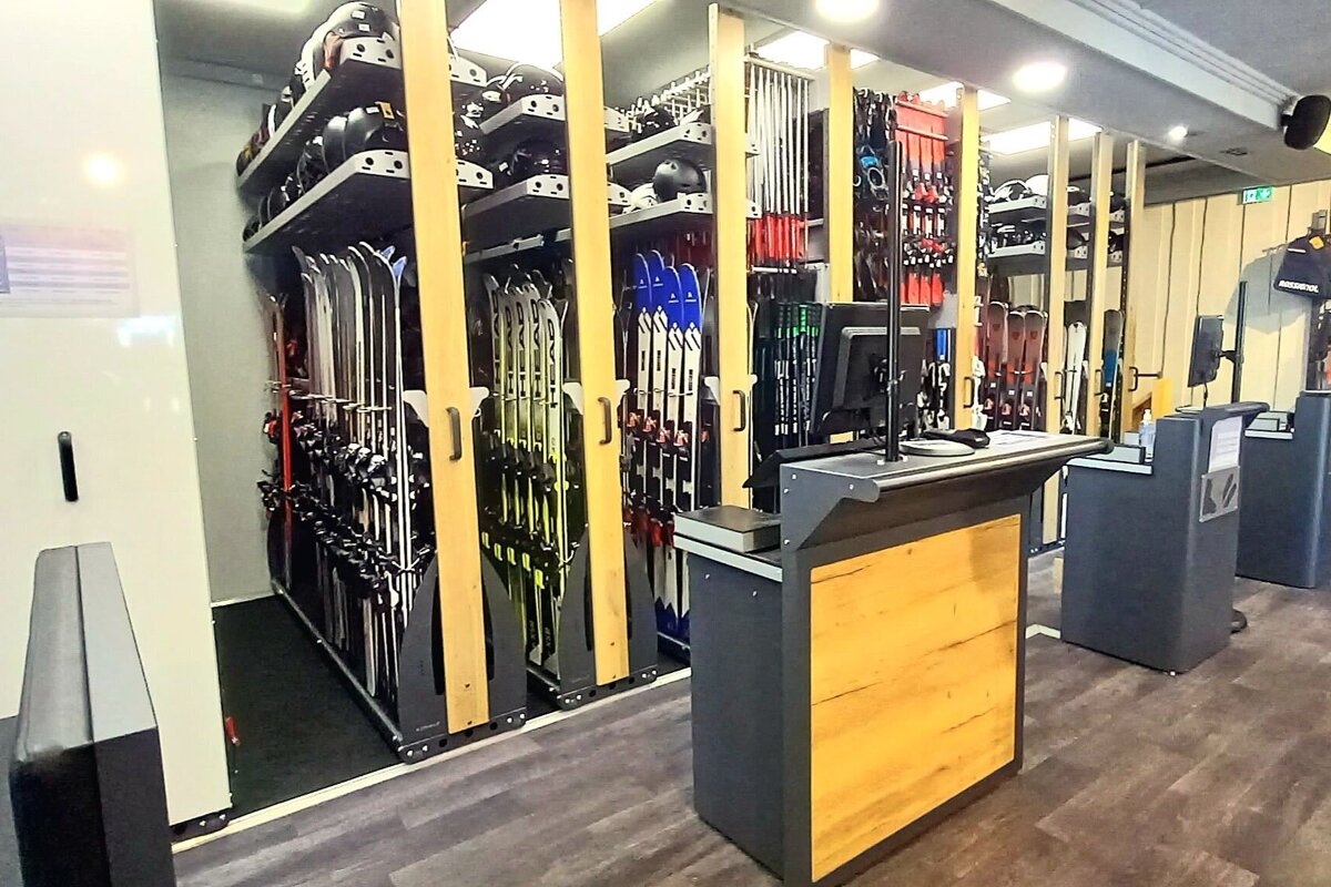 An organized ski rental shop with numerous skis, poles, and helmets displayed on wall racks, alongside several modern service counters.