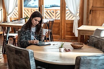 A woman sits at a table with a cup of coffee and a tablet