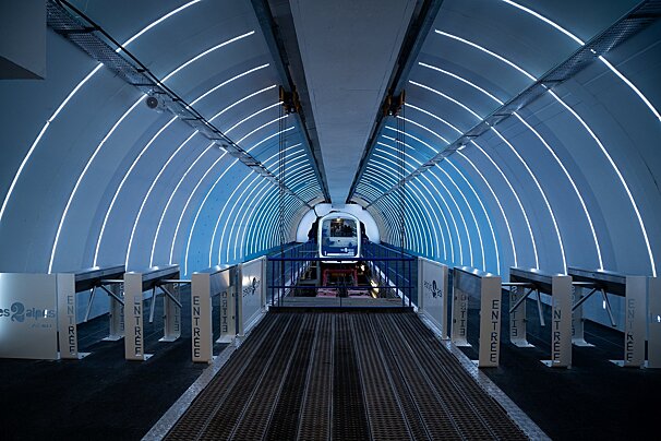 A futuristic, blue-lit tunnel station with curved LED lights, where a sleek funicular awaits beyond 