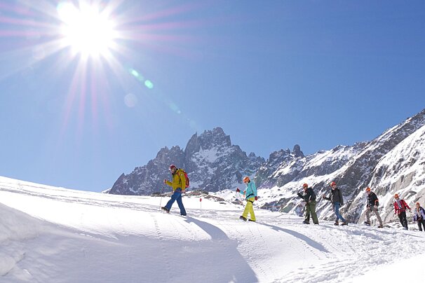A group of people walking in the snow with mountains in the background