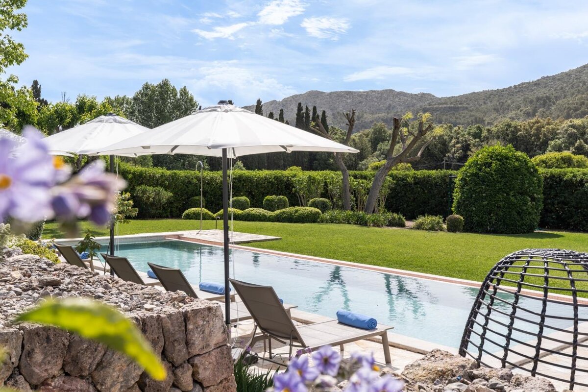 A swimming pool surrounded by chairs and umbrellas with mountains in the background