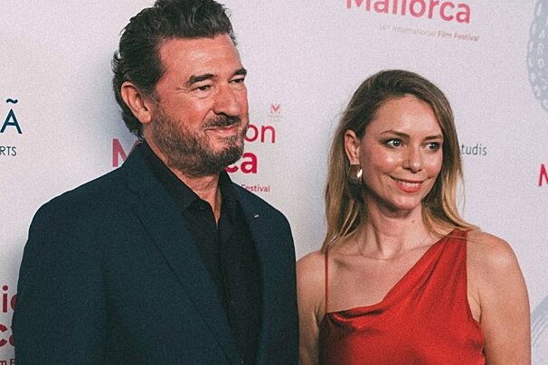 A smiling bearded man in a dark suit and a woman in a red dress pose together at the Mallorca International Film Festival.