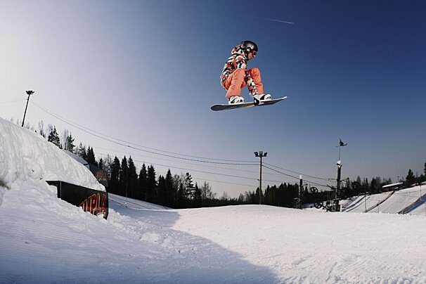 A snowboarder is jumping in the air near a sign that says ' a ' on it