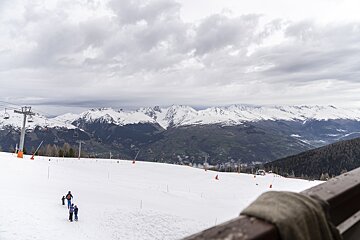 People skiing down a snowy slope with mountains in the background