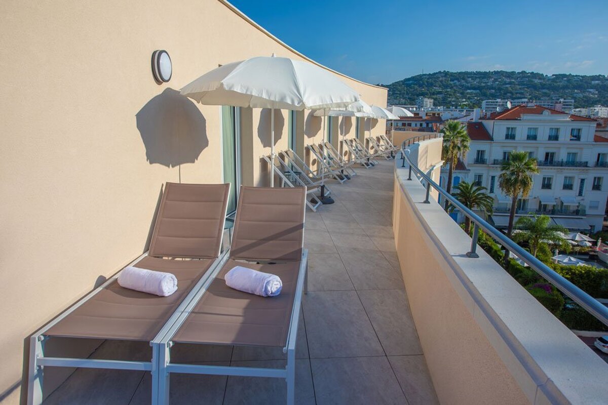 A balcony with a row of lounge chairs and umbrellas