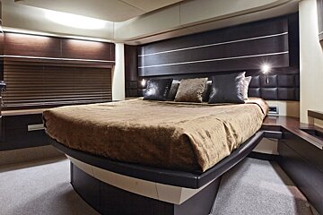 A sleek, modern bedroom inside a boat or yacht, featuring a large bed with brown bedding, dark wood paneling, and subtle lighting.