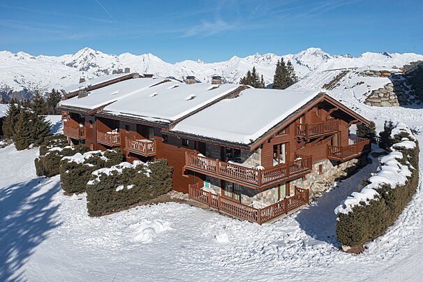 A snow covered building with a balcony and mountains in the background