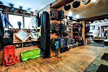 A retail store packed with winter sports and outdoor gear, including helmets, clothing, backpacks, and sleds, set in a rustic wooden interior.