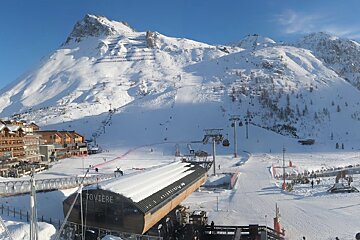 A vibrant ski resort scene with majestic snow-covered mountains, charming chalet buildings, busy ski slopes, various ski lifts, and the Toviere station.
