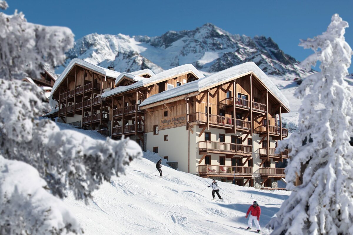 Skiers are skiing down a snowy slope in front of a building that says village montagne
