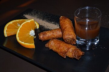 image of some chocolate spring rolls, with orange slices and a glass of bitter