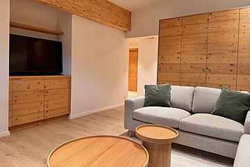 Modern living room featuring light wood floors & accents, a grey sofa with green pillows, wood tables, and a built-in TV.