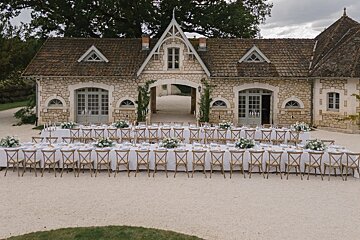 A very long table with chairs in front of a stone building