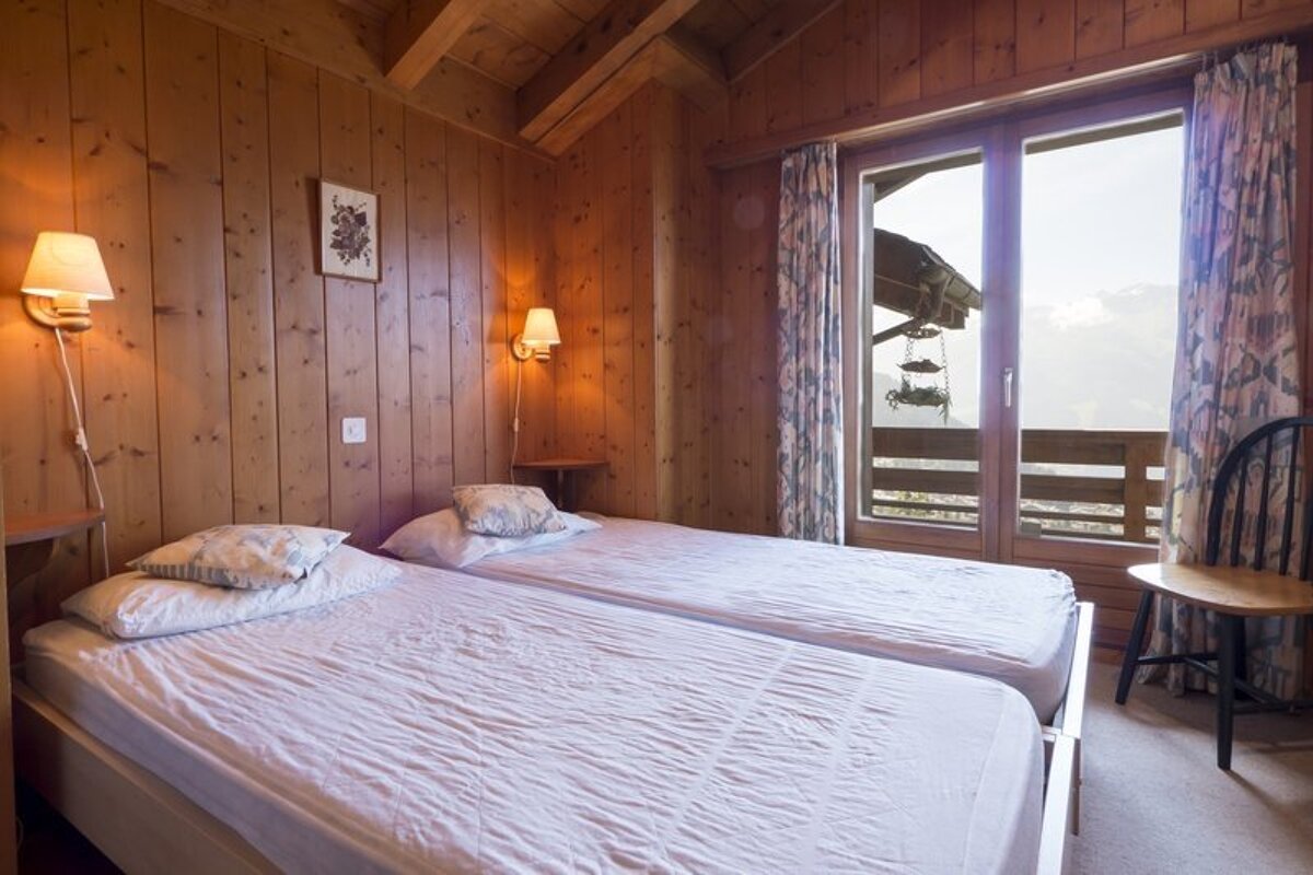 A cozy, wood-paneled bedroom with twin beds and a glass door leading to a balcony with mountain views.