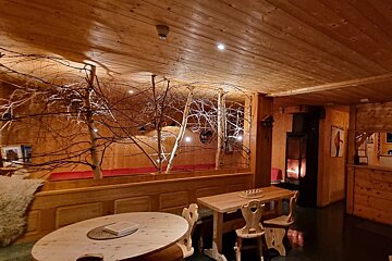 A cozy, wood-paneled room with rustic wooden furniture, decorative trees, and a warm fireplace, creating an inviting, cabin-like ambiance.