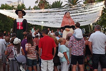 a parade at a fiesta with two giant statues being carried