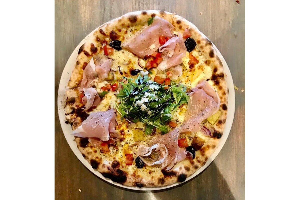 A pizza with ham and vegetables on a white plate