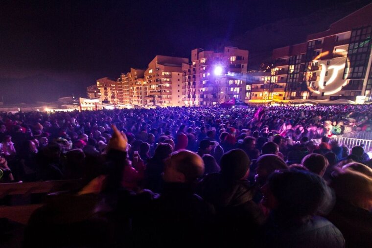 A large crowd of people watching a concert with a building in the background