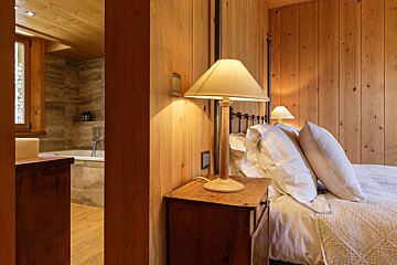 A bedroom with a lamp on a nightstand next to a bed