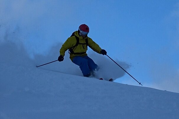 A man in a yellow jacket is skiing down a snowy hill